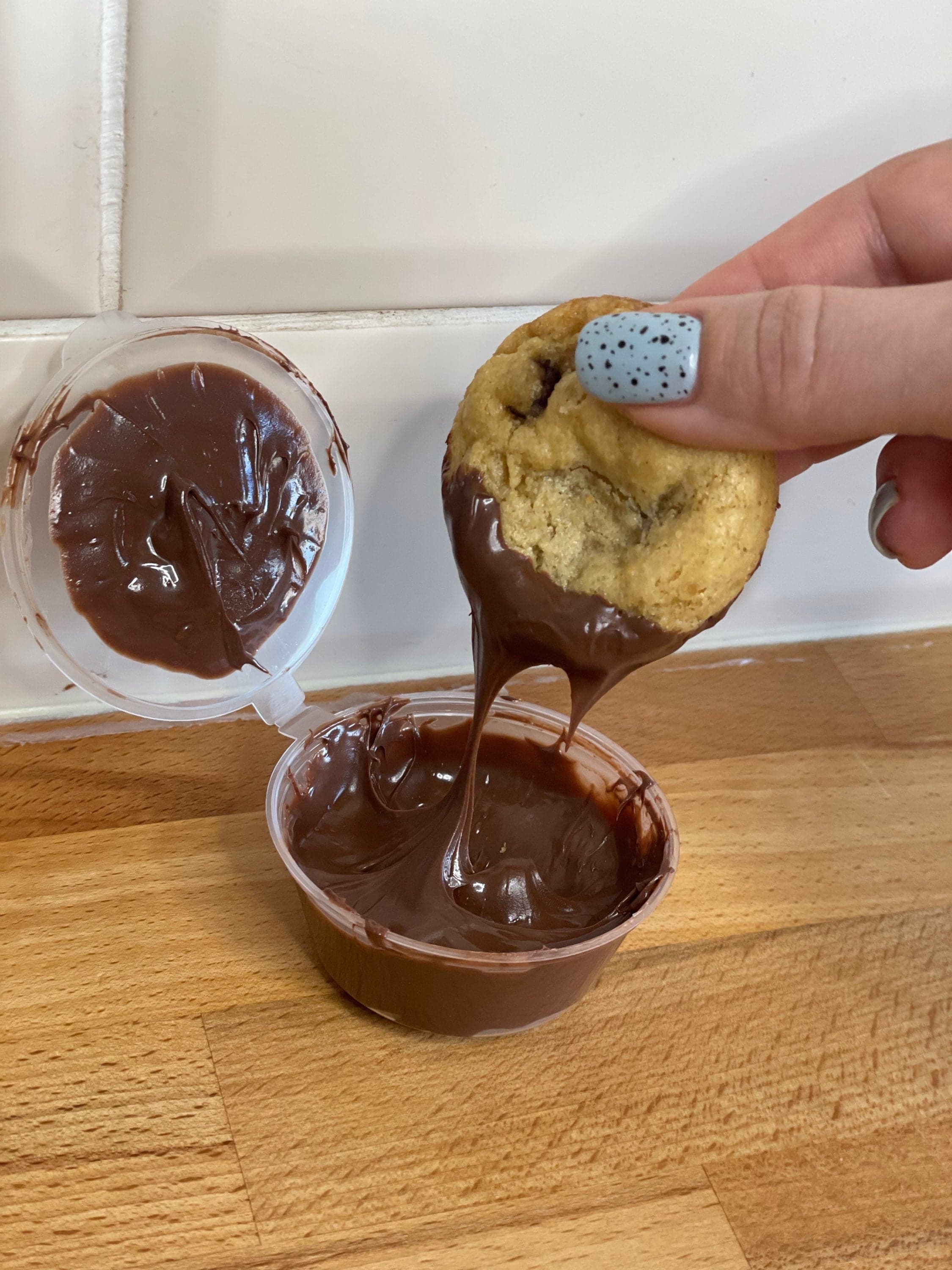 A cookie being dipped into a pot of glossy chocolate