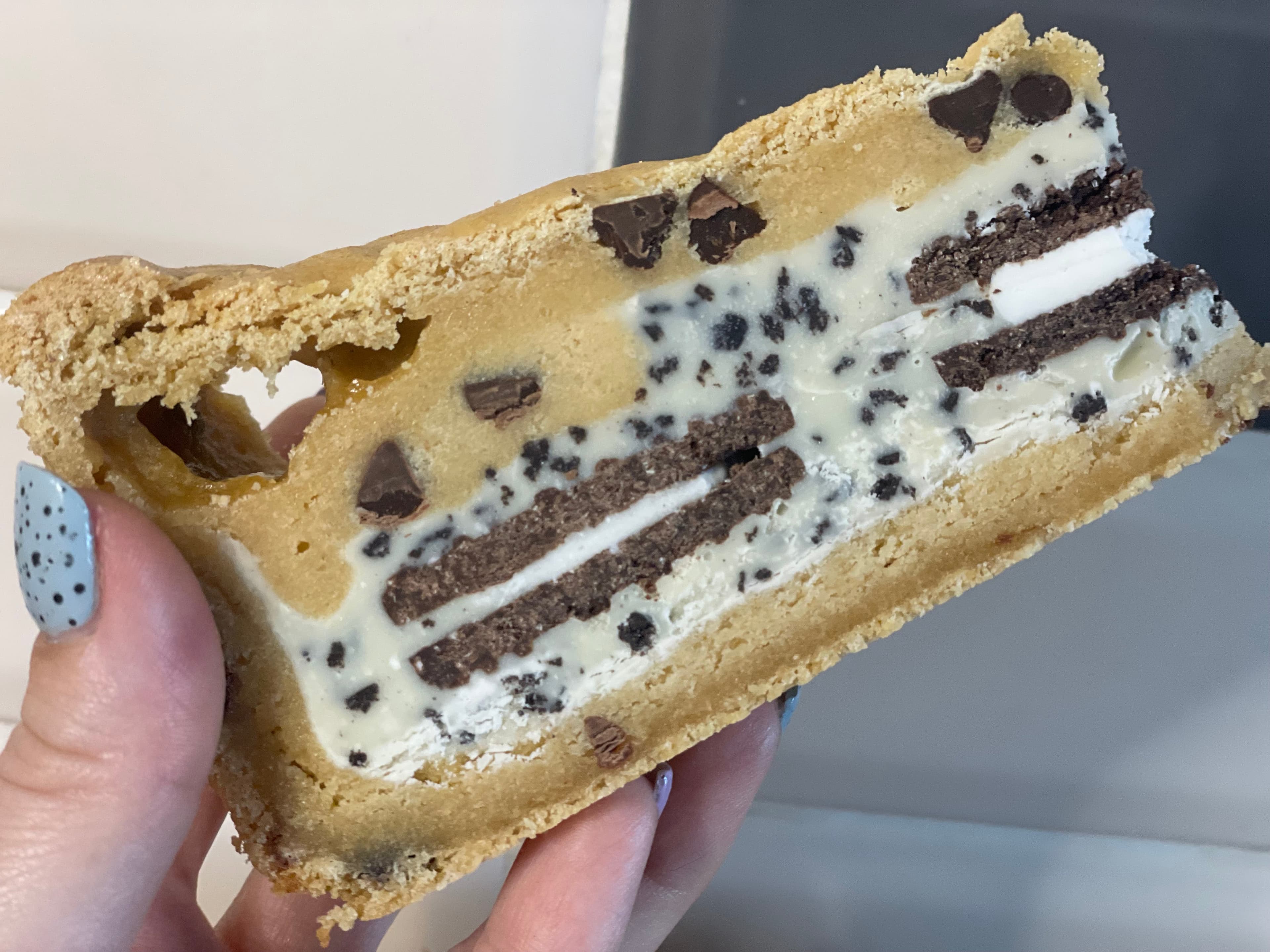 Cookies and cream cookie pie slice held in a hand, layered with cream and chocolate biscuit